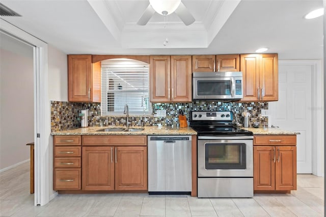 kitchen featuring appliances with stainless steel finishes, decorative backsplash, light stone counters, a tray ceiling, and sink