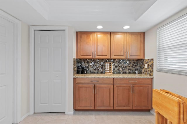 kitchen featuring light stone counters, a raised ceiling, backsplash, and light tile patterned floors