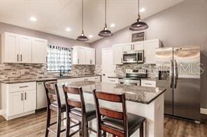 kitchen featuring stainless steel appliances, dark wood-type flooring, white cabinetry, and a kitchen bar