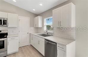 kitchen featuring tasteful backsplash, a sink, light countertops, appliances with stainless steel finishes, and light wood finished floors