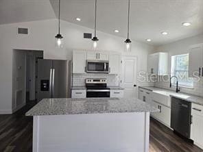 kitchen featuring white cabinets, vaulted ceiling, appliances with stainless steel finishes, and decorative light fixtures