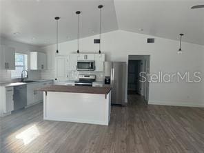 kitchen with white cabinets, sink, stainless steel appliances, a center island, and vaulted ceiling