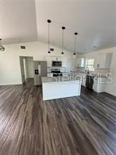 kitchen featuring vaulted ceiling, light countertops, a kitchen island with sink, decorative light fixtures, and dark wood finished floors