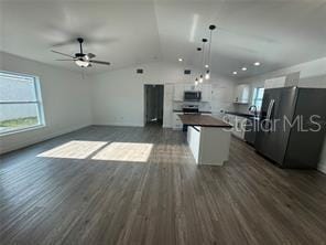 kitchen with dark wood-type flooring, a ceiling fan, a center island, appliances with stainless steel finishes, and lofted ceiling