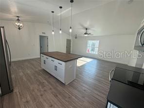 kitchen featuring white cabinetry, vaulted ceiling, ceiling fan with notable chandelier, stainless steel refrigerator, and a center island