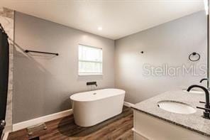 bathroom featuring a freestanding tub, vanity, curtained shower, wood finished floors, and baseboards