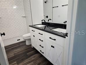 bathroom with vanity, a tile shower, toilet, and wood finished floors
