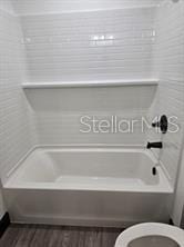 bathroom featuring toilet, shower / tub combination, and wood finished floors