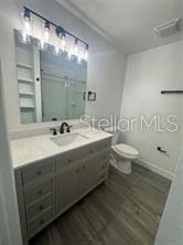 bathroom with hardwood / wood-style floors, walk in shower, vanity, and toilet