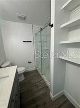 bathroom with hardwood / wood-style flooring, walk in shower, vanity, and toilet