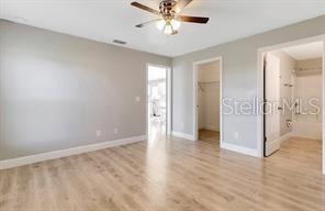 unfurnished bedroom with light wood-type flooring, a closet, baseboards, and a walk in closet