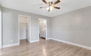 unfurnished bedroom with a closet, baseboards, ensuite bathroom, a walk in closet, and wood finished floors