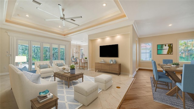 living room featuring ceiling fan with notable chandelier, light wood-type flooring, crown molding, and a raised ceiling