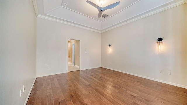 empty room with a raised ceiling, ornamental molding, and hardwood / wood-style flooring