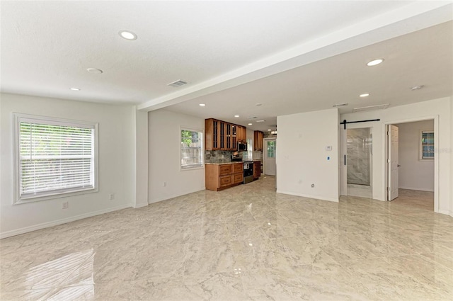 unfurnished living room featuring a barn door and a healthy amount of sunlight