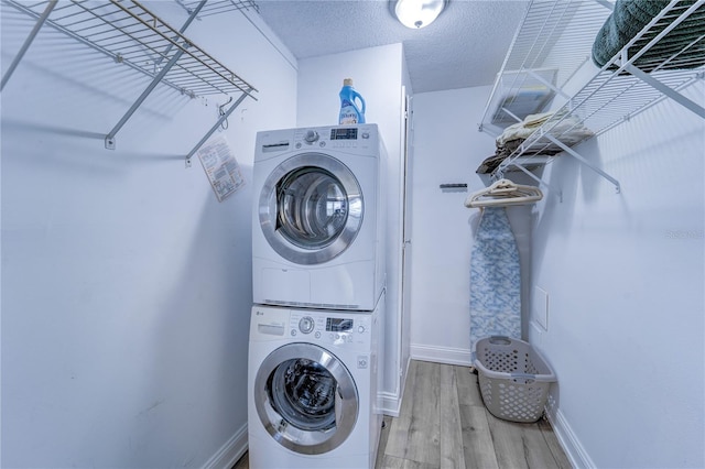 clothes washing area with a textured ceiling, stacked washer and dryer, and hardwood / wood-style floors