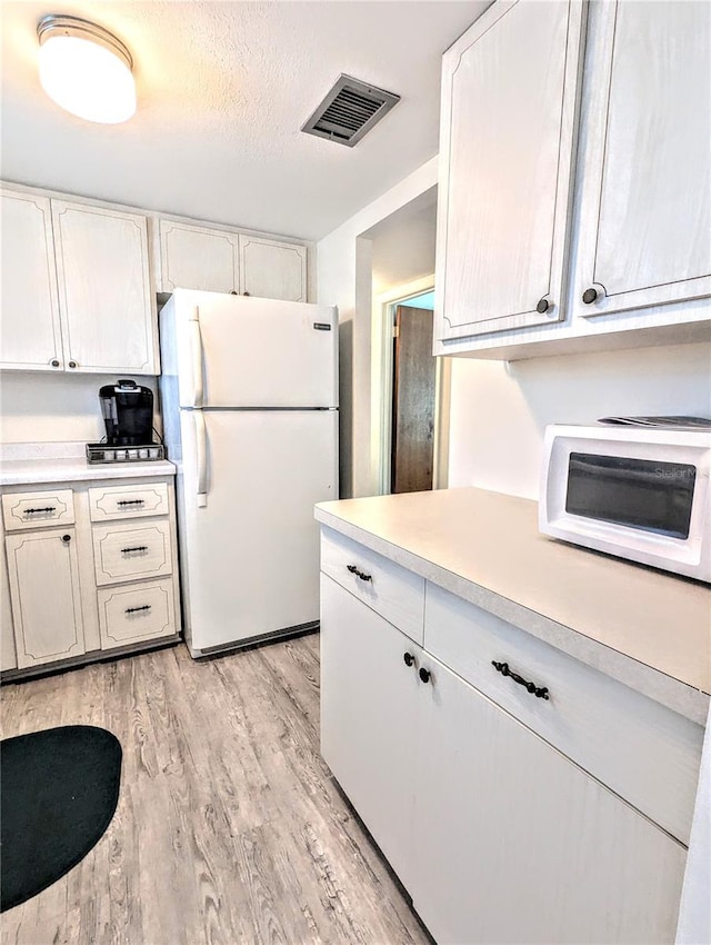 kitchen with a textured ceiling, light wood-type flooring, white fridge, and white cabinetry