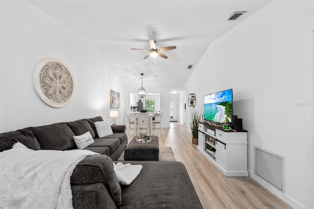 living room with light wood-type flooring, ceiling fan with notable chandelier, and lofted ceiling