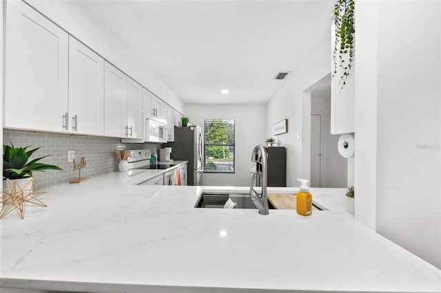 kitchen with light stone counters, sink, kitchen peninsula, white cabinetry, and appliances with stainless steel finishes