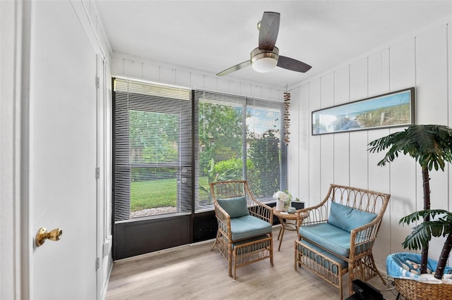 living area with light wood-type flooring, wood walls, and ceiling fan