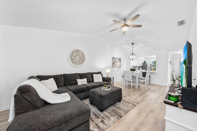 living room featuring ceiling fan with notable chandelier, vaulted ceiling, and light hardwood / wood-style flooring