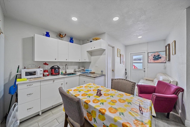 kitchen with a textured ceiling, light wood-type flooring, sink, and white cabinetry