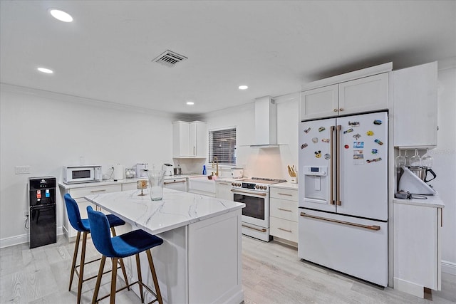 kitchen with light stone counters, light hardwood / wood-style floors, white cabinetry, wall chimney exhaust hood, and white appliances