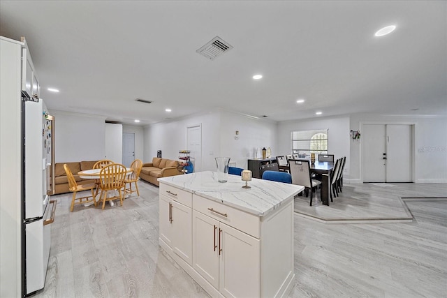 kitchen featuring white refrigerator, white cabinets, a kitchen island, light hardwood / wood-style flooring, and light stone countertops