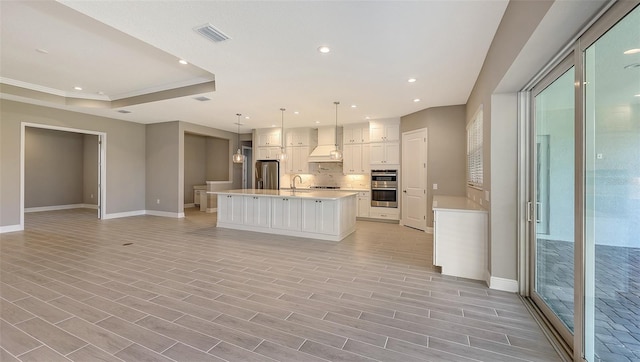 kitchen with custom exhaust hood, a raised ceiling, decorative light fixtures, a large island, and stainless steel appliances