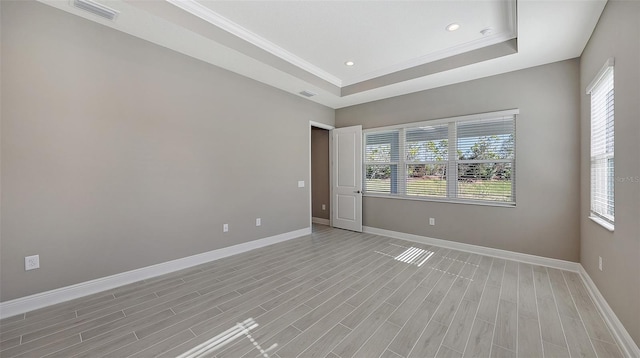 spare room with a raised ceiling, light hardwood / wood-style flooring, and ornamental molding