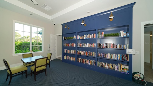 recreation room with dark colored carpet, built in shelves, and a tray ceiling