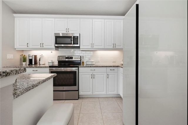 kitchen featuring light tile patterned floors, tasteful backsplash, light stone counters, white cabinets, and appliances with stainless steel finishes