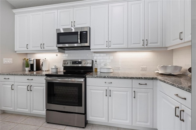 kitchen with white cabinetry, light tile patterned floors, dark stone counters, and appliances with stainless steel finishes