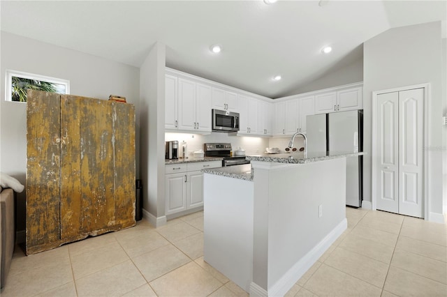 kitchen with stainless steel appliances, light stone counters, an island with sink, vaulted ceiling, and white cabinets