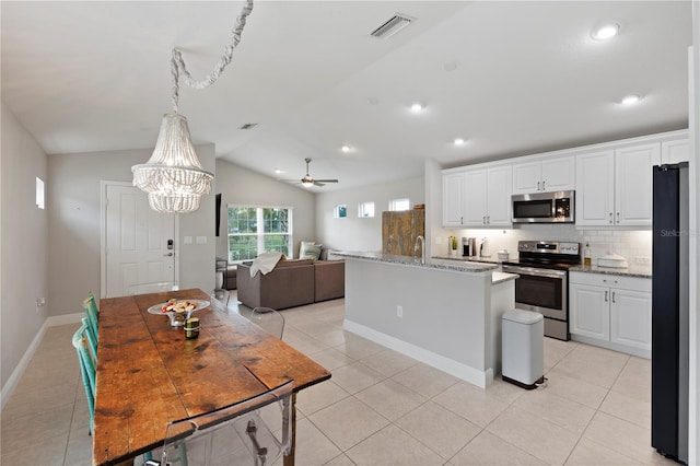 kitchen with light stone countertops, appliances with stainless steel finishes, ceiling fan with notable chandelier, vaulted ceiling, and white cabinets