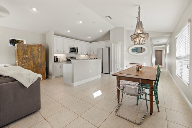 kitchen featuring hanging light fixtures, stainless steel appliances, light tile patterned floors, lofted ceiling, and white cabinets