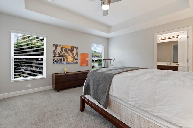 carpeted bedroom with a raised ceiling, connected bathroom, and ceiling fan