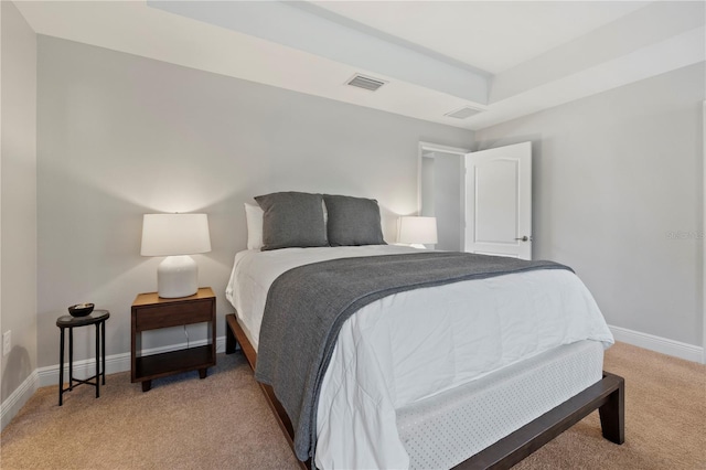 bedroom with a raised ceiling and light colored carpet