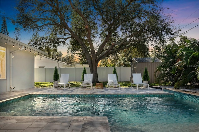 pool at dusk featuring a patio and a storage unit