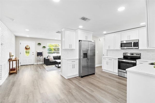 kitchen with white cabinets, light stone counters, appliances with stainless steel finishes, and light hardwood / wood-style flooring