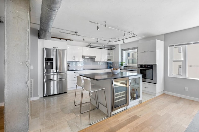 kitchen with beverage cooler, a center island, stainless steel appliances, white cabinets, and light hardwood / wood-style flooring