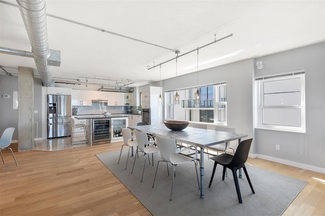 dining area with wine cooler, track lighting, and light hardwood / wood-style flooring