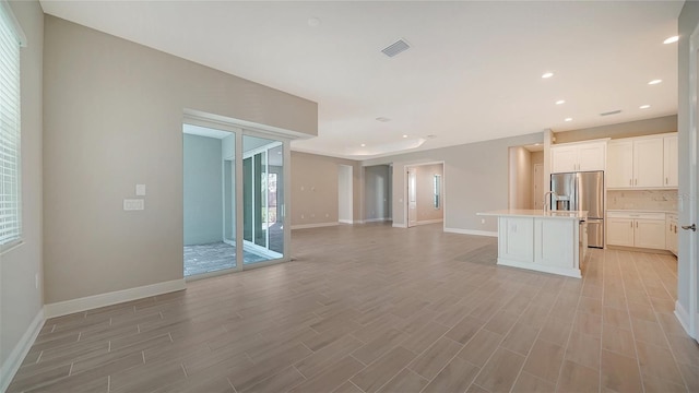 interior space featuring backsplash, white cabinetry, stainless steel refrigerator with ice dispenser, a center island, and light hardwood / wood-style floors