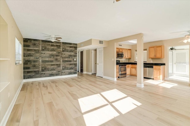 unfurnished living room with wooden walls, ceiling fan, and light hardwood / wood-style flooring