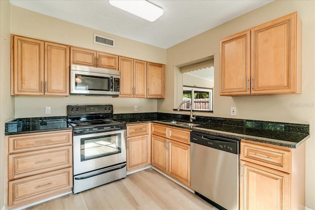 kitchen with sink, a textured ceiling, stainless steel appliances, dark stone countertops, and light wood-type flooring