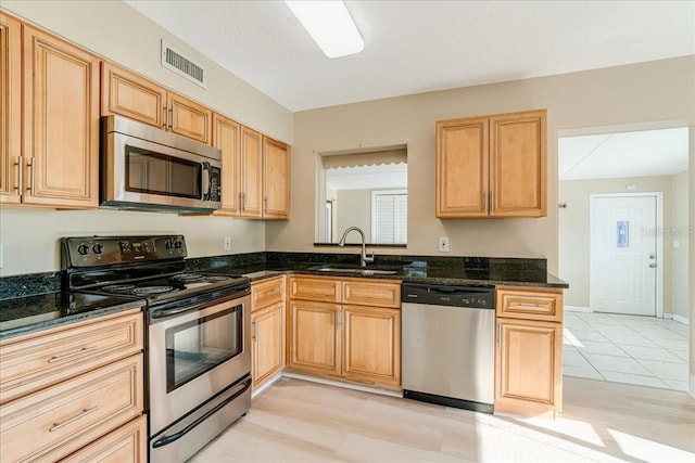 kitchen with light hardwood / wood-style floors, stainless steel appliances, sink, and dark stone counters