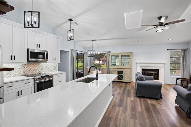 kitchen with sink, a high end fireplace, white cabinetry, appliances with stainless steel finishes, and ceiling fan with notable chandelier