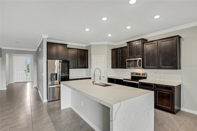 kitchen with an island with sink, light tile patterned flooring, sink, stainless steel appliances, and crown molding