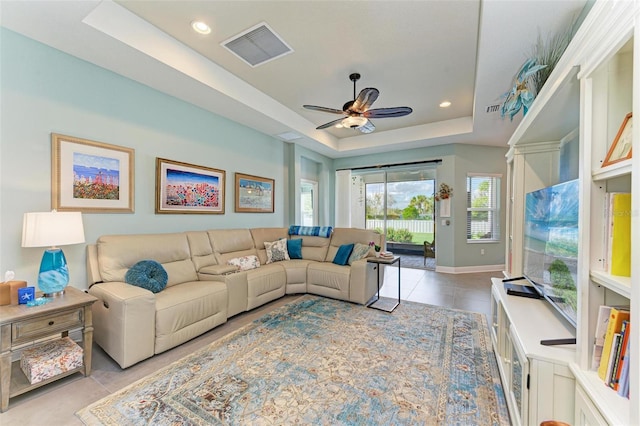 living room with a raised ceiling, ceiling fan, and light tile patterned flooring