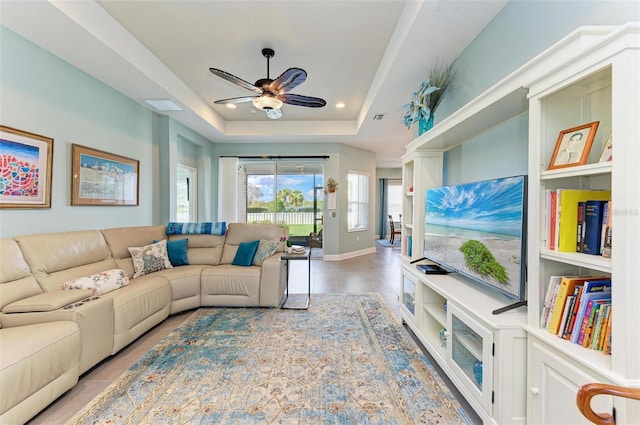 living room featuring a raised ceiling and ceiling fan